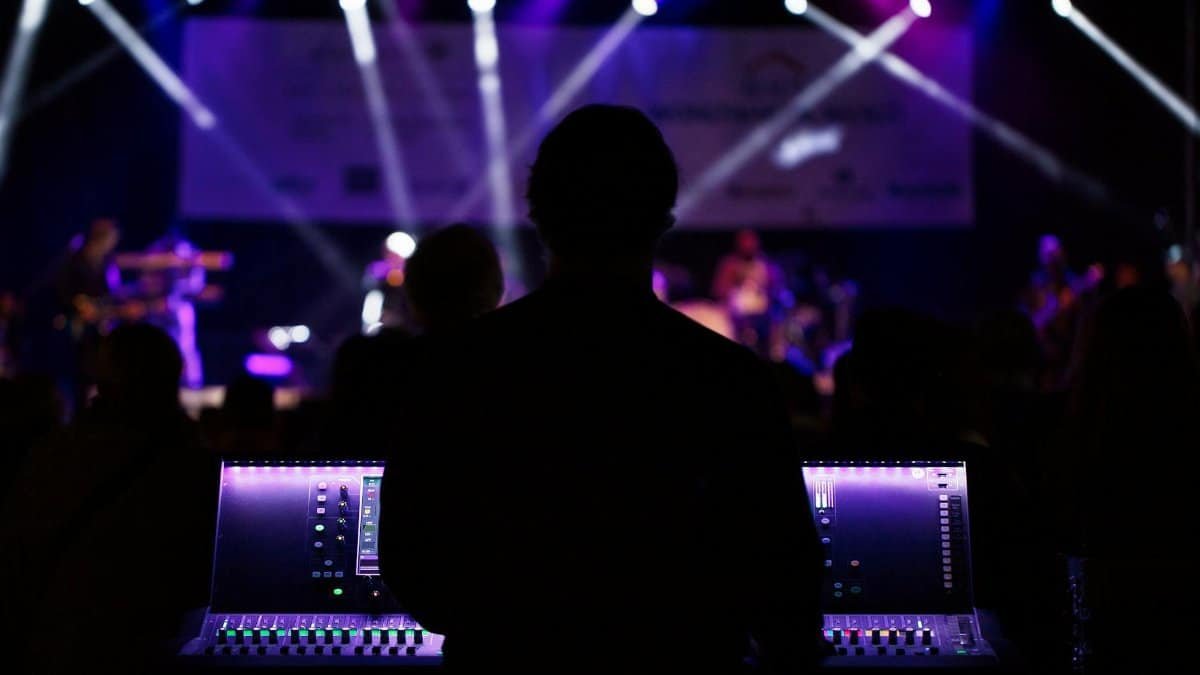 A sound engineer manages the audio mixer during a vibrant live concert with colorful lighting.