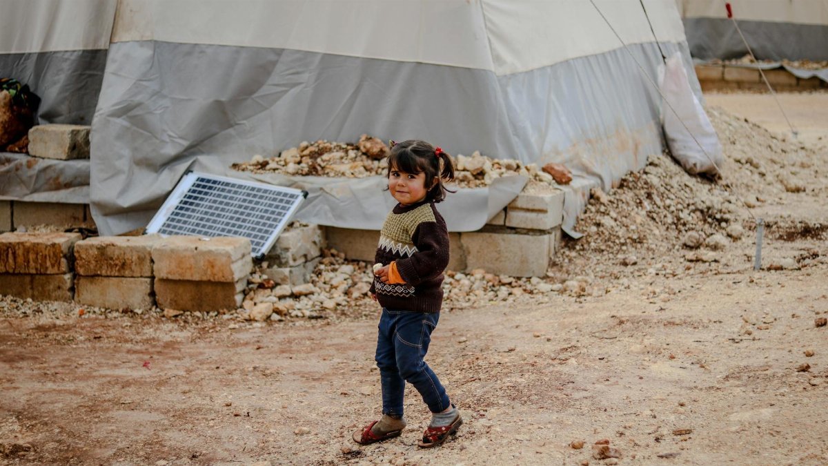 A young girl smiles in a refugee camp in Idlib, Syria, amidst temporary shelters.