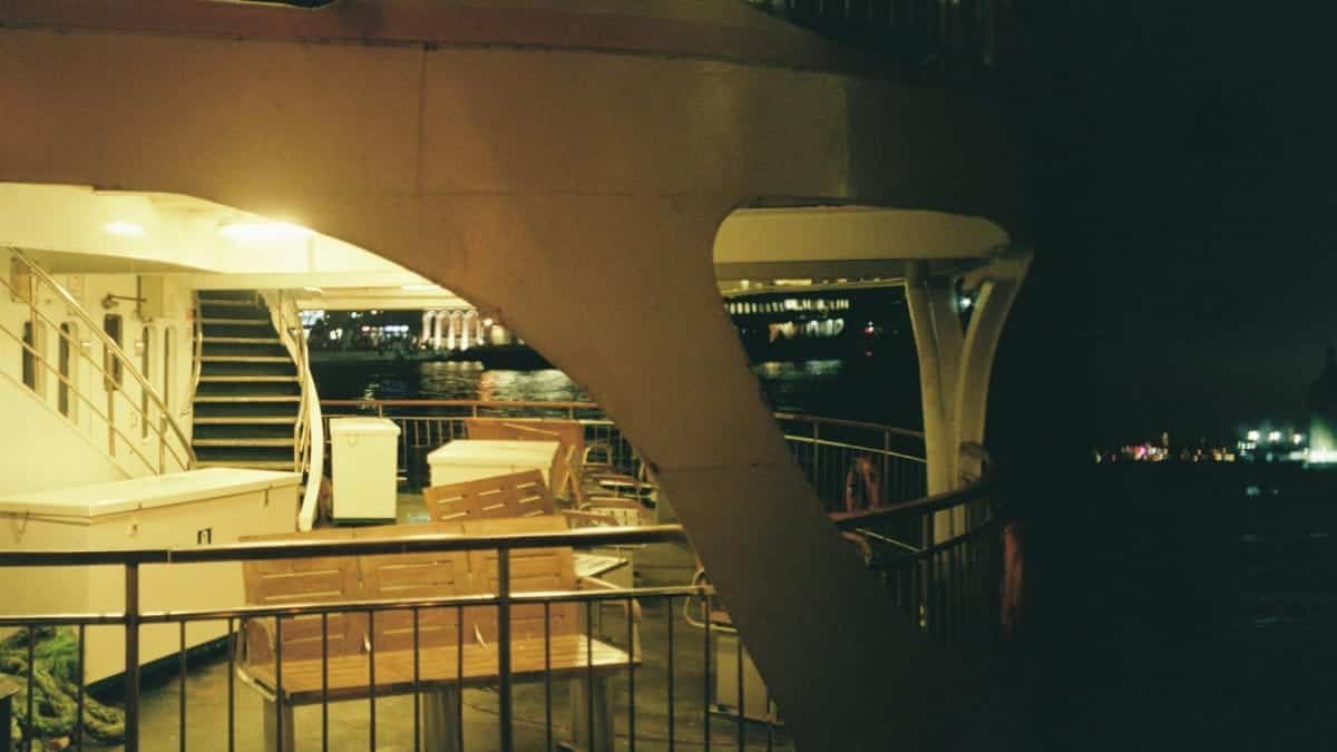 Empty ferry deck at night with city lights reflecting over water.