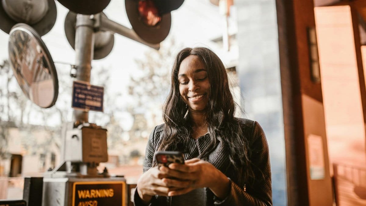 Woman happily using her smartphone outdoors near railway signals, capturing a moment of leisure and connectivity.