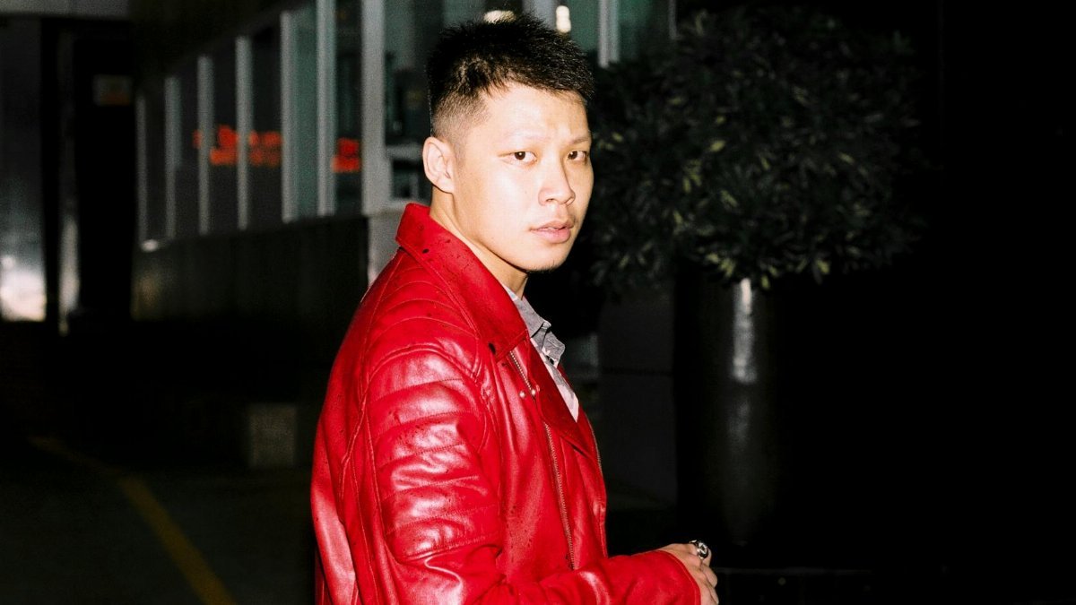 A man wearing a bright red jacket standing outdoors at night in an urban setting in Ho Chi Minh City.