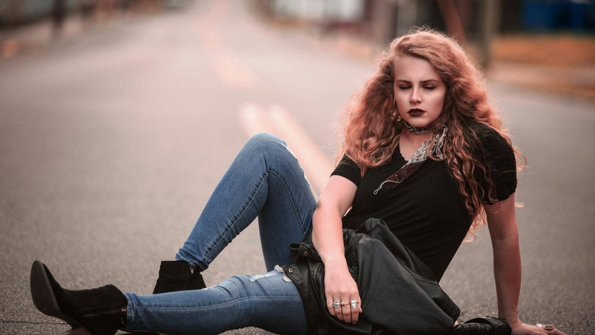 Young woman with curly hair sitting confidently on a city street in casual wear, Cleveland TN.