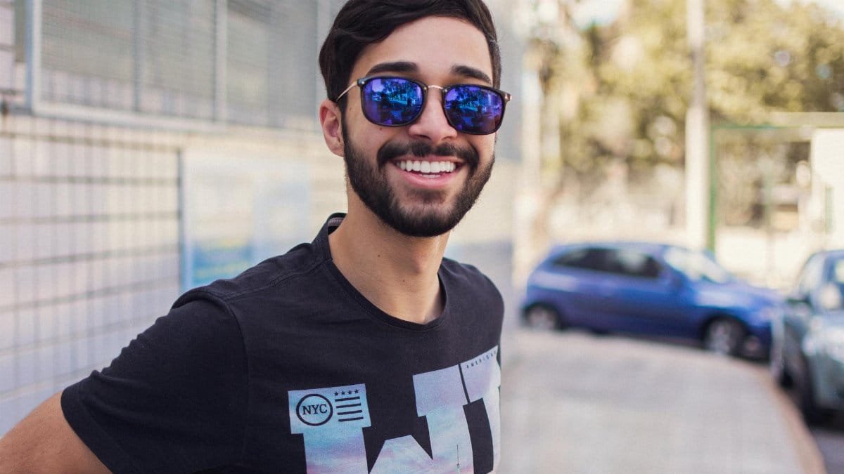 Portrait of a smiling man wearing sunglasses outdoors, showcasing modern fashion and style.
