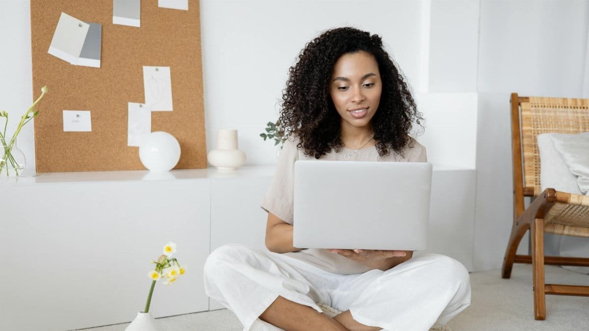 Young woman with curly hair working on her laptop in a cozy home setting, exuding confidence and focus.