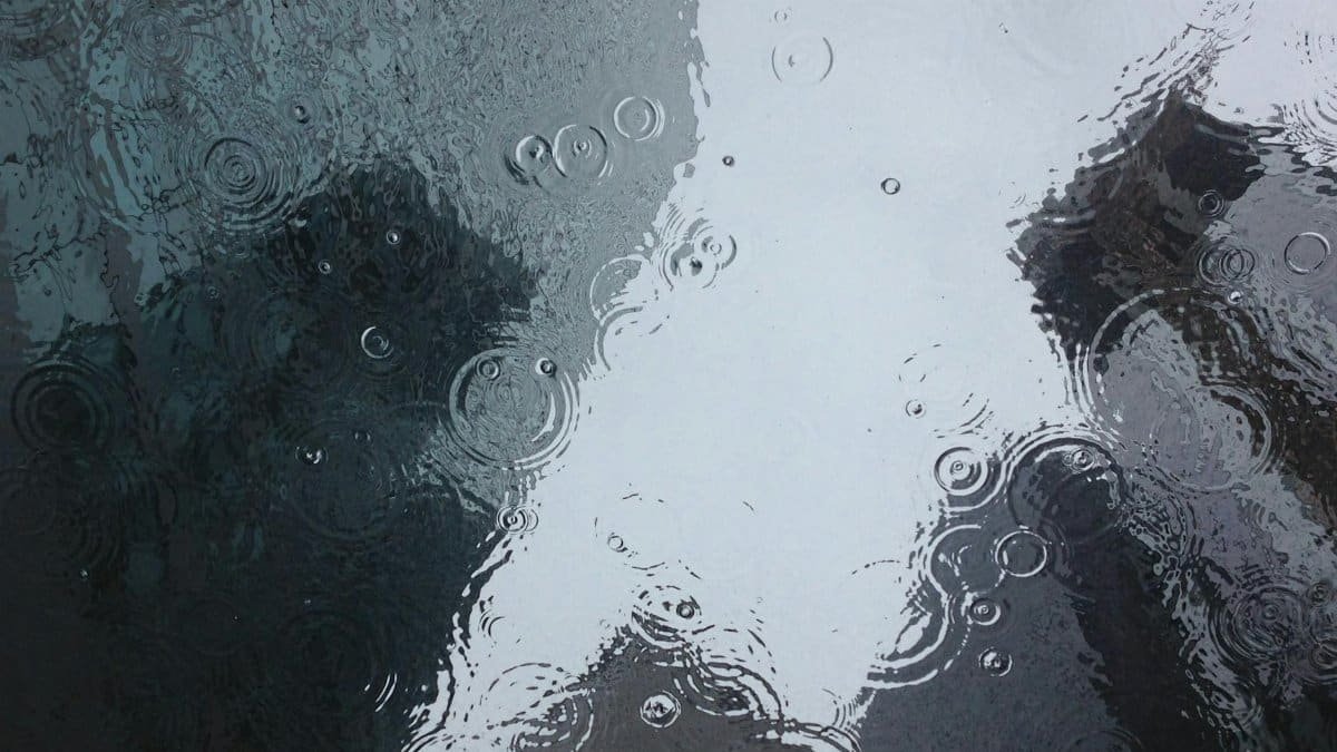 Raindrops create ripples on a window, reflecting an urban backdrop.