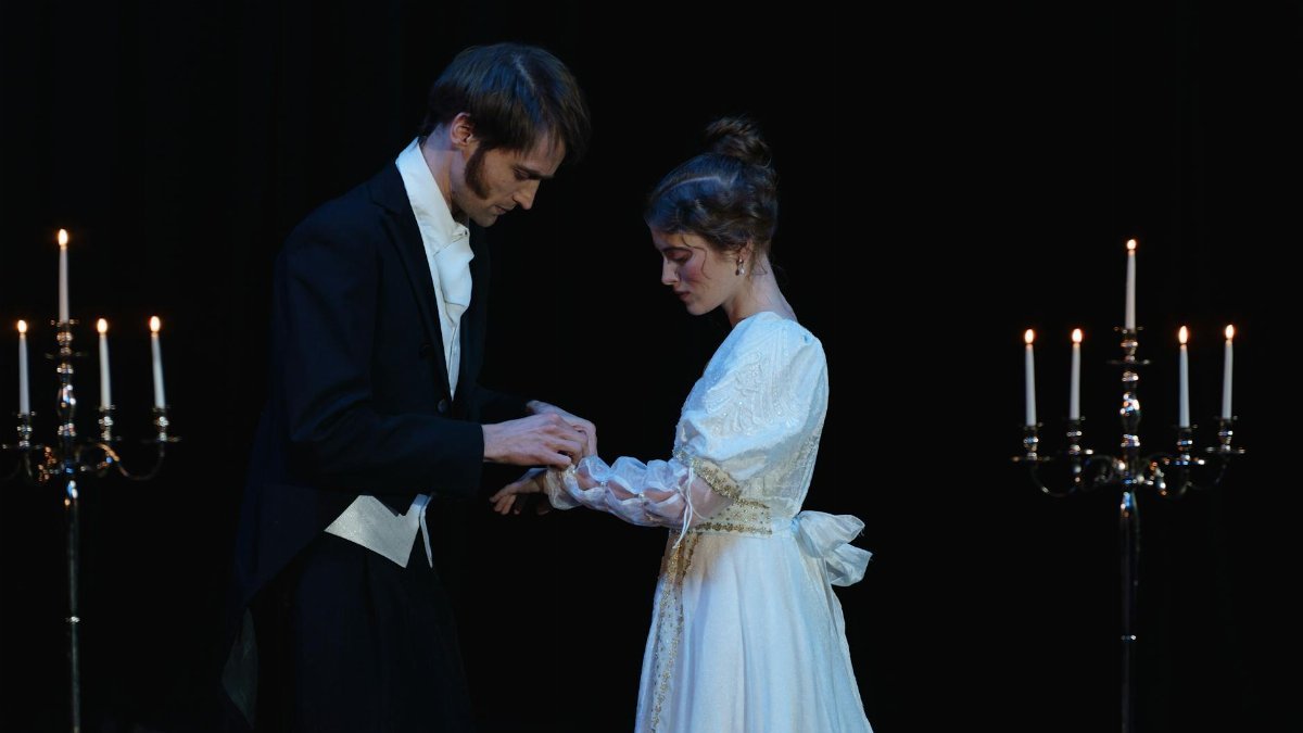 A dramatic scene depicting a romantic moment between two actors on stage.