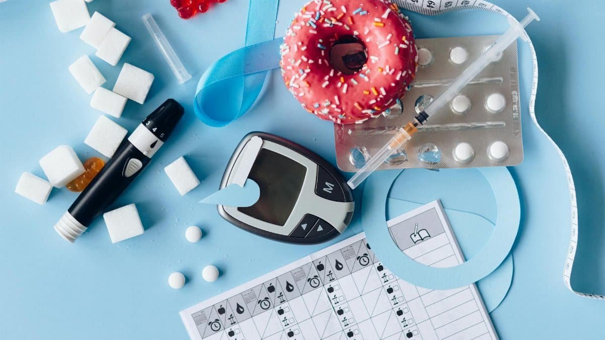Still life image of diabetes management equipment, sweets, and medication arranged artfully on a blue background.