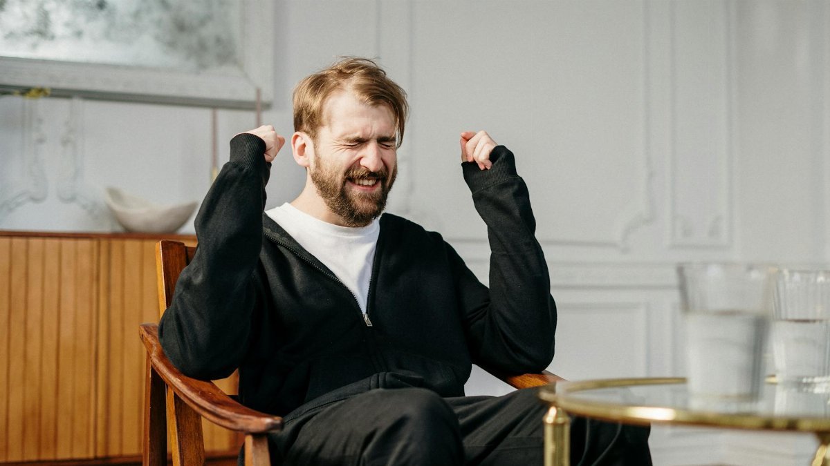 A bearded man expressing emotional distress in a modern interior setting, seeking mental health support.