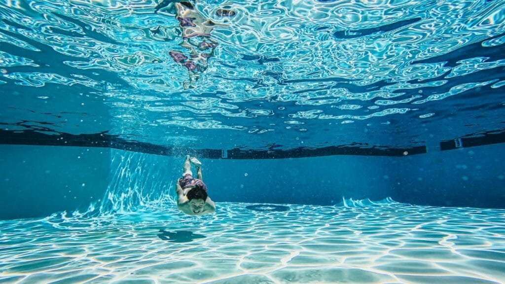 Underwater photo capturing a boy swimming in a clear blue pool, creating ripples.