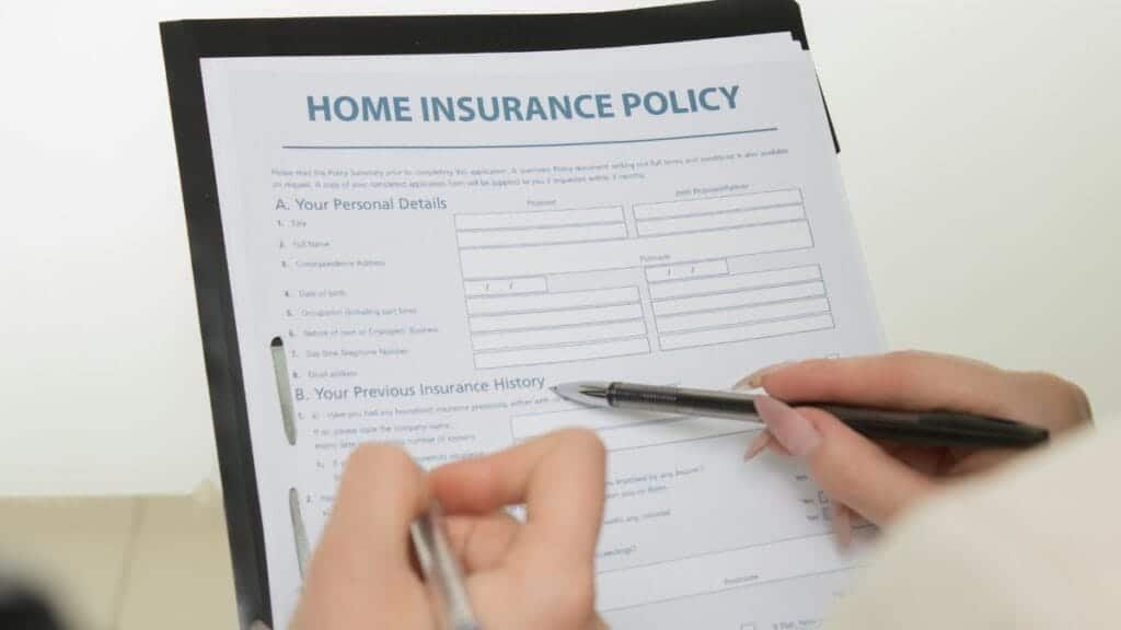 Hands holding pens filling out a home insurance policy document for coverage details.