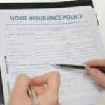 Hands holding pens filling out a home insurance policy document for coverage details.