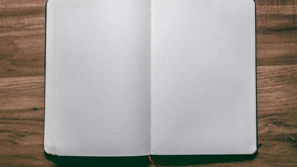 A top-down view of an open blank notebook on a wooden desk, perfect for design or writing projects.