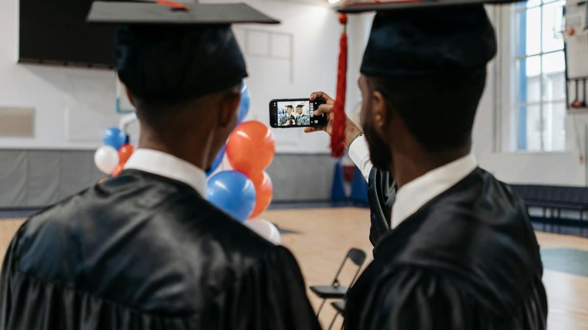 Two graduates in caps and gowns taking a selfie indoors, celebrating their achievement.