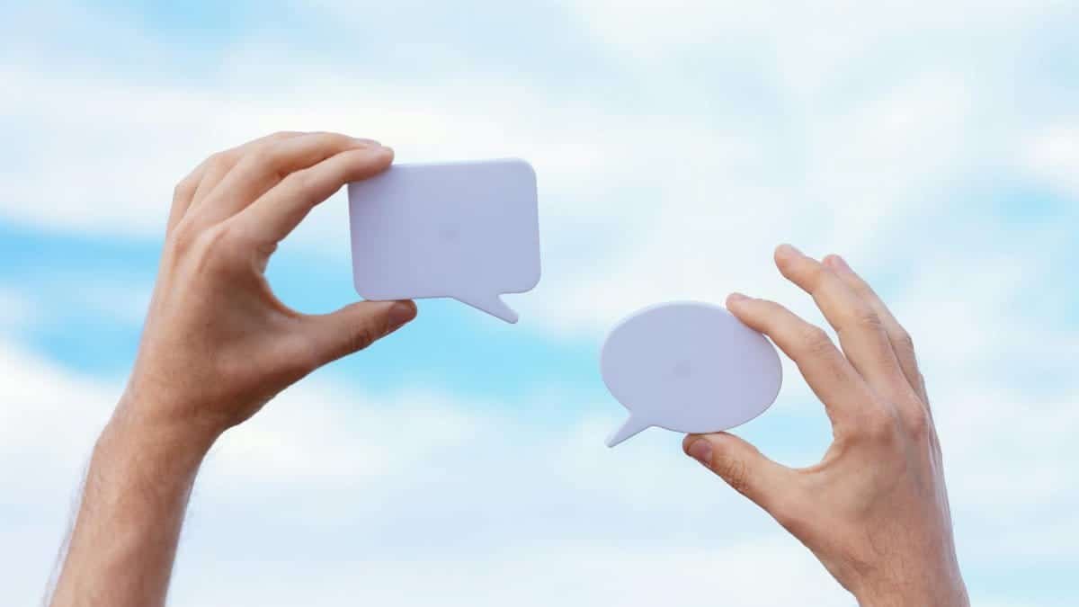 Close-up of hands holding speech bubbles, symbolizing communication and dialogue against a blue sky.