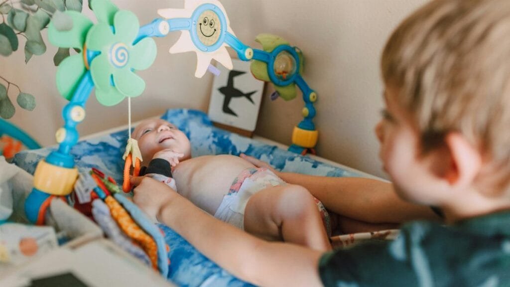 A cute baby lying in a crib, engaged with colorful hanging toys, depicting joyful childhood moments.