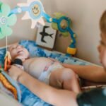 A cute baby lying in a crib, engaged with colorful hanging toys, depicting joyful childhood moments.