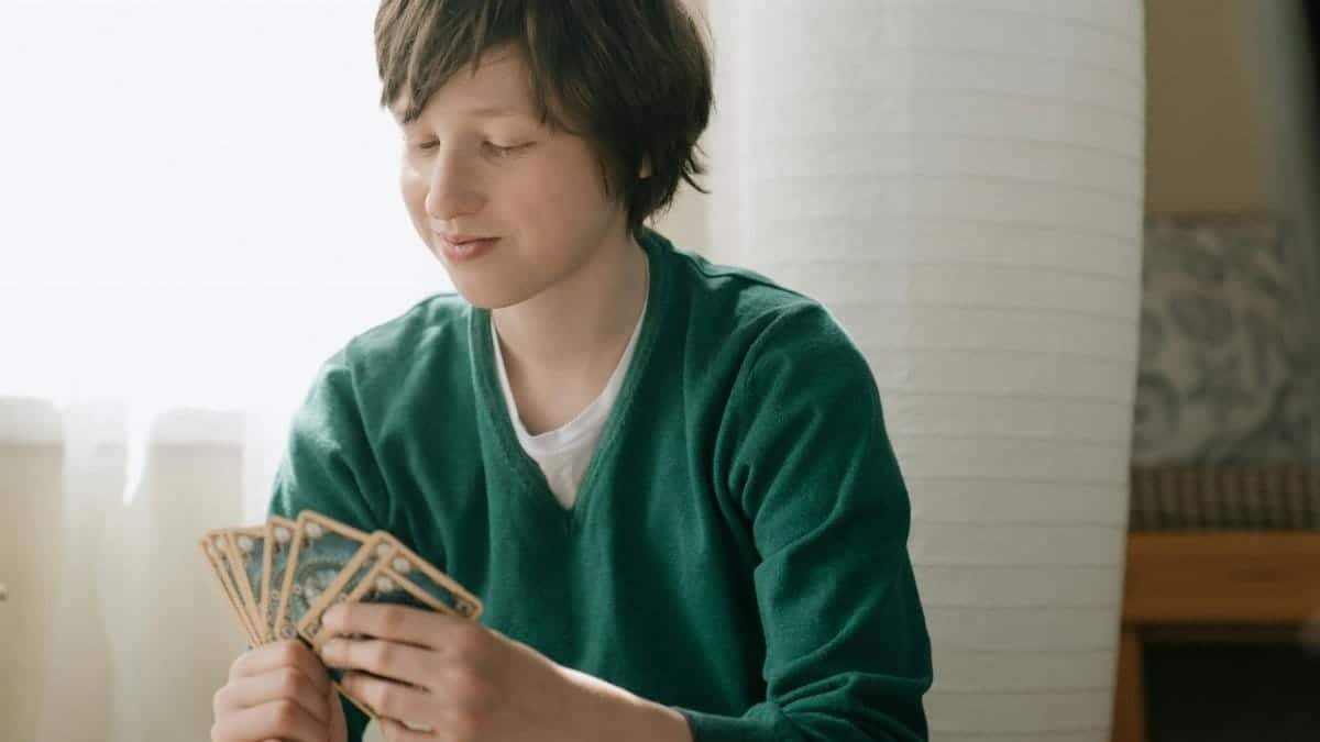Teenager in green sweater smiling while playing a strategic card game indoors.