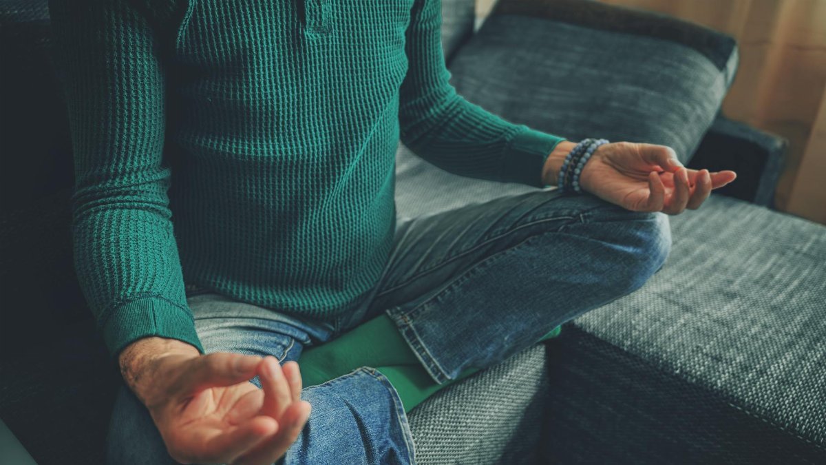 Close-up of a person meditating at home, cross-legged on a couch, emphasizing relaxation and mindfulness.