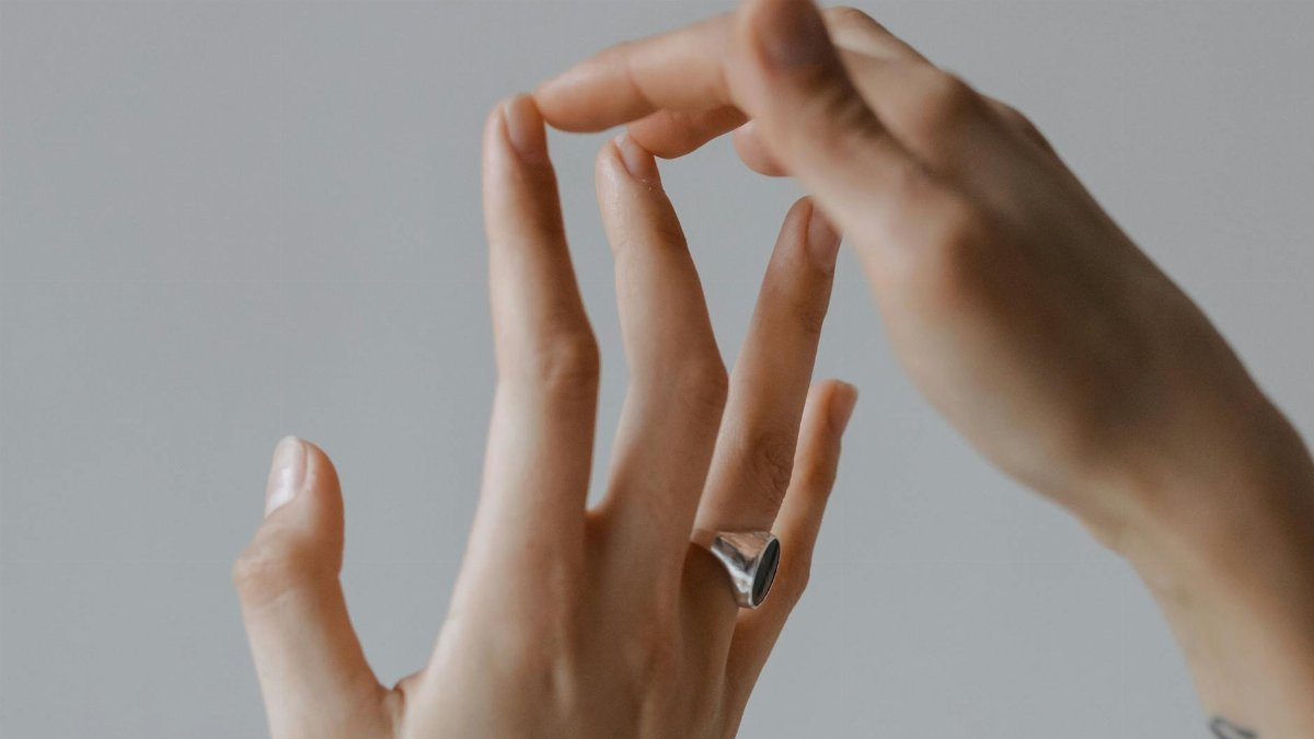 Artistic close-up of human hands with a focus on a ring and gentle touch gesture.