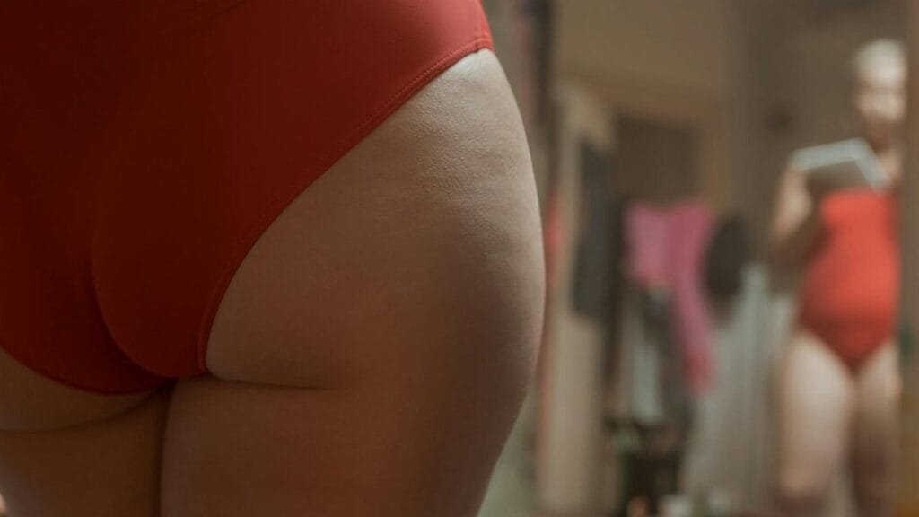 A close-up view of a person embracing body positivity in red swimwear, self-reflecting in a mirror.