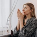 A woman meditates peacefully indoors, seeking relaxation and inner peace through mindful practices.