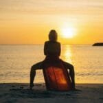 A woman in a red dress performs yoga at sunset on a serene beach.