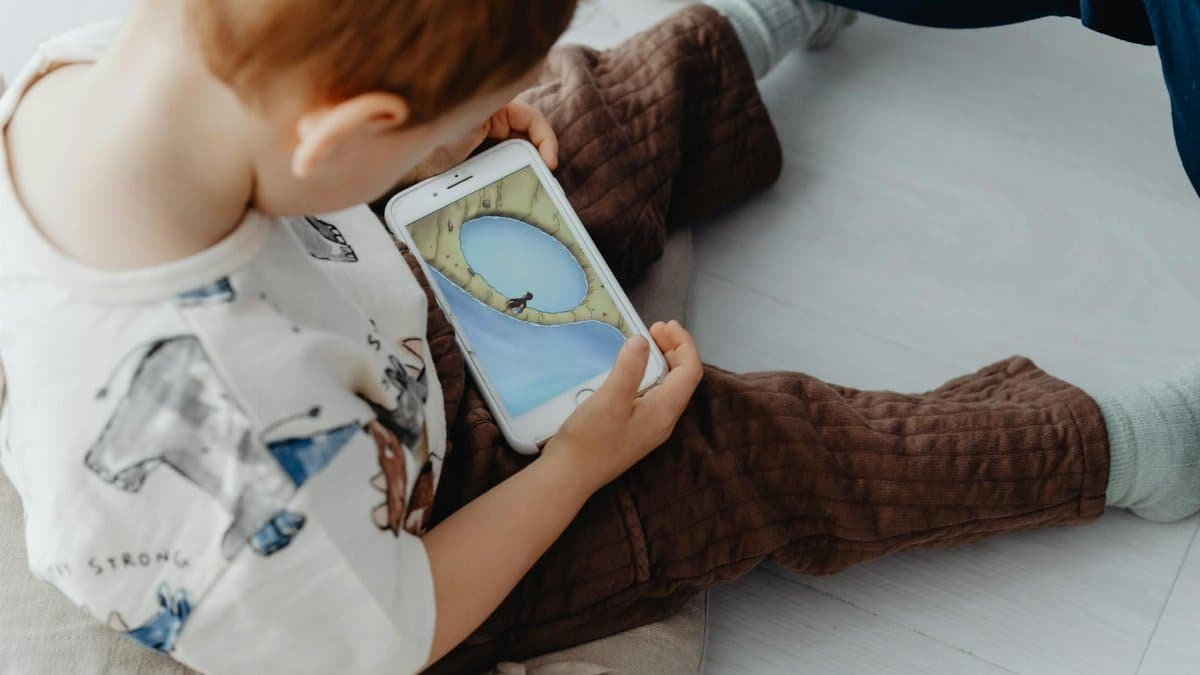 A young child playing an educational game on a smartphone indoors, focused on learning.