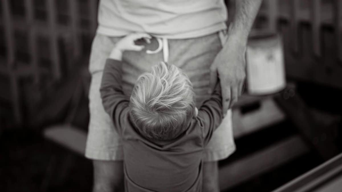 A touching black and white close-up of a young boy hugging his father's legs, capturing a heartwarming bond.