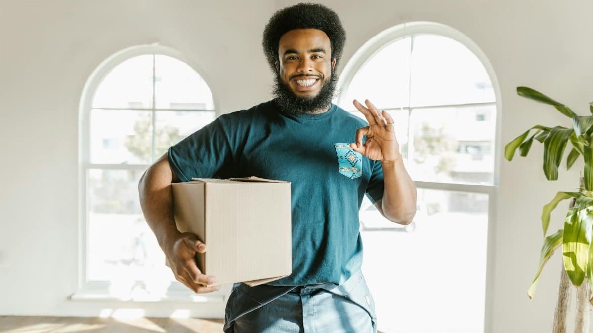 Happy man carrying a moving box in a brightly lit new home, symbolizing a fresh start.