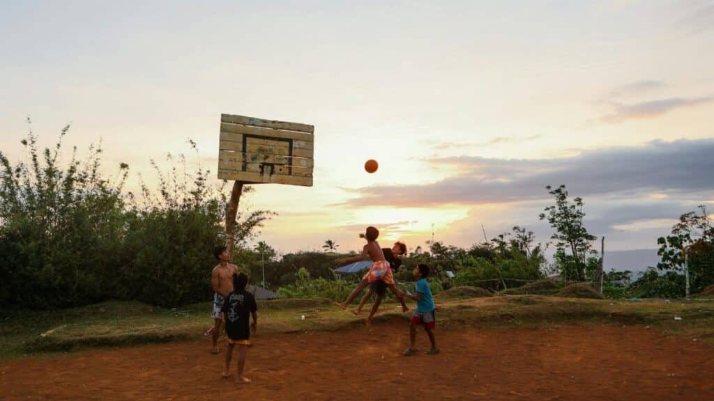 Four kids engaged in a lively basketball game on a rustic outdoor court at sunset.