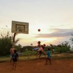 Four kids engaged in a lively basketball game on a rustic outdoor court at sunset.