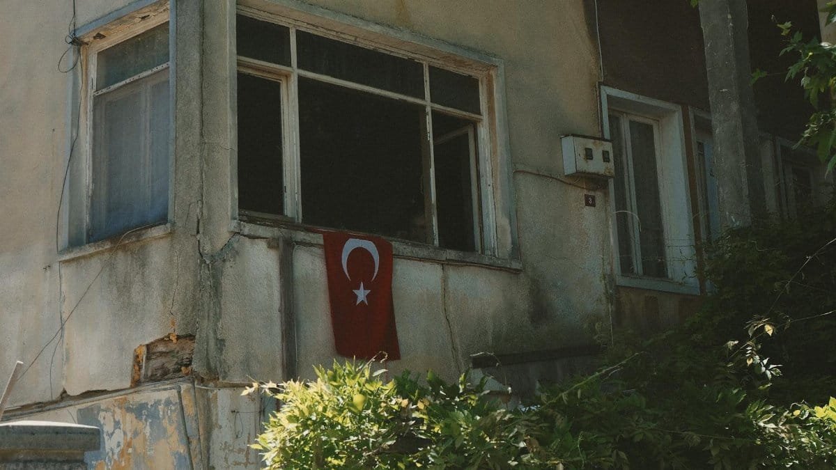 A worn-out building facade featuring a Turkish flag in the window, showcasing national pride.