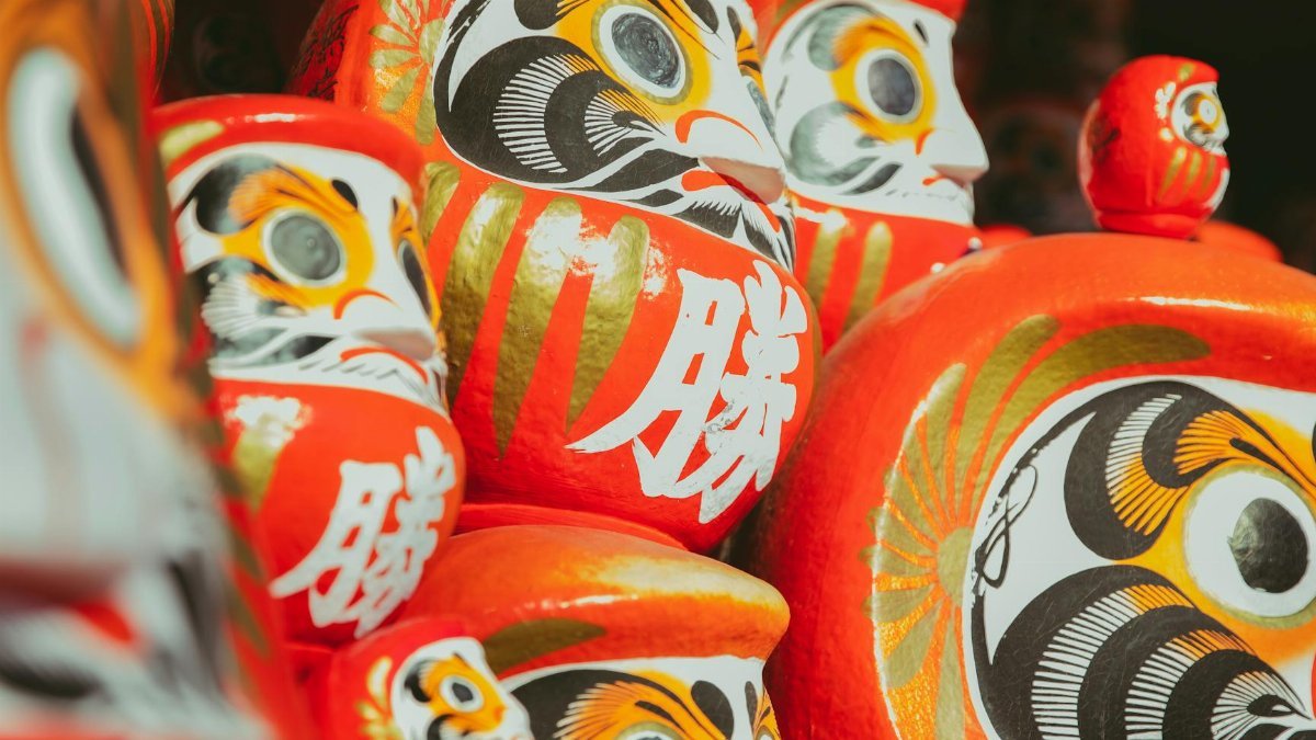 Collection of traditional Japanese red painted daruma dolls depicting bearded man stacked together on local market on street in city