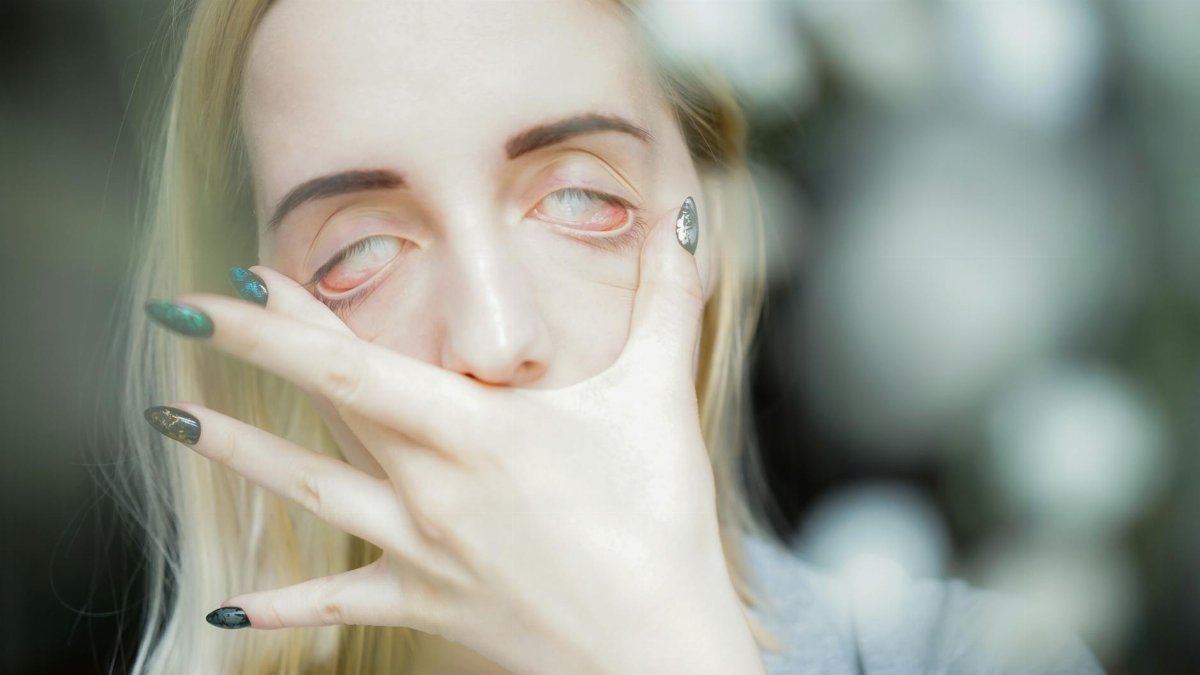 Young female with short blond hair touching face with hand with manicure and rolling eyes
