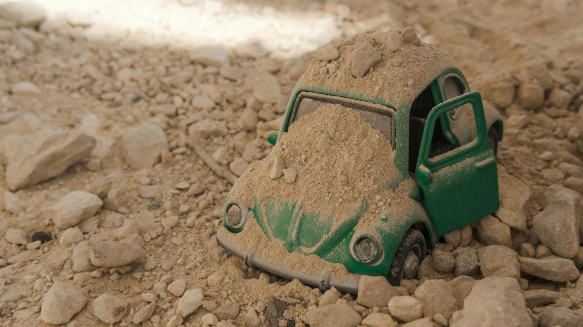 Close-up of a toy car partially buried in sand and gravel, depicting outdoor play and exploration.