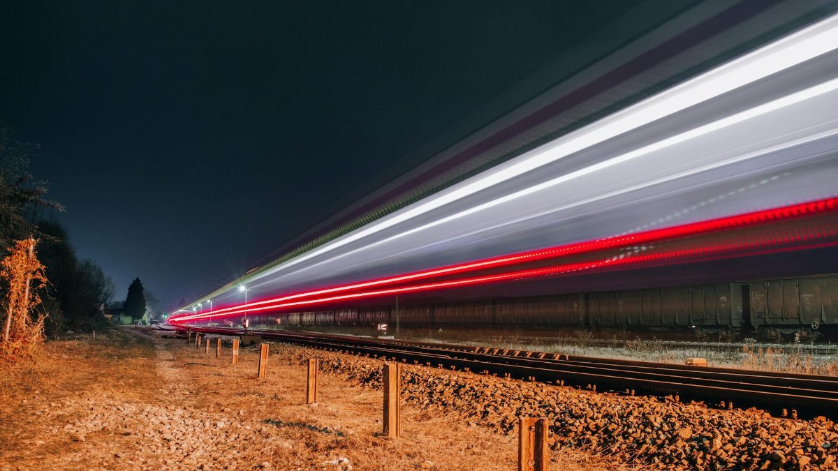 Long exposure of a train creating vivid light trails on a nighttime railway track.