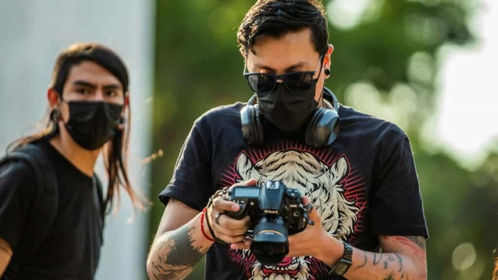 A photographer wearing a face mask checks his camera in Mexico City outdoors.