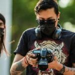 A photographer wearing a face mask checks his camera in Mexico City outdoors.