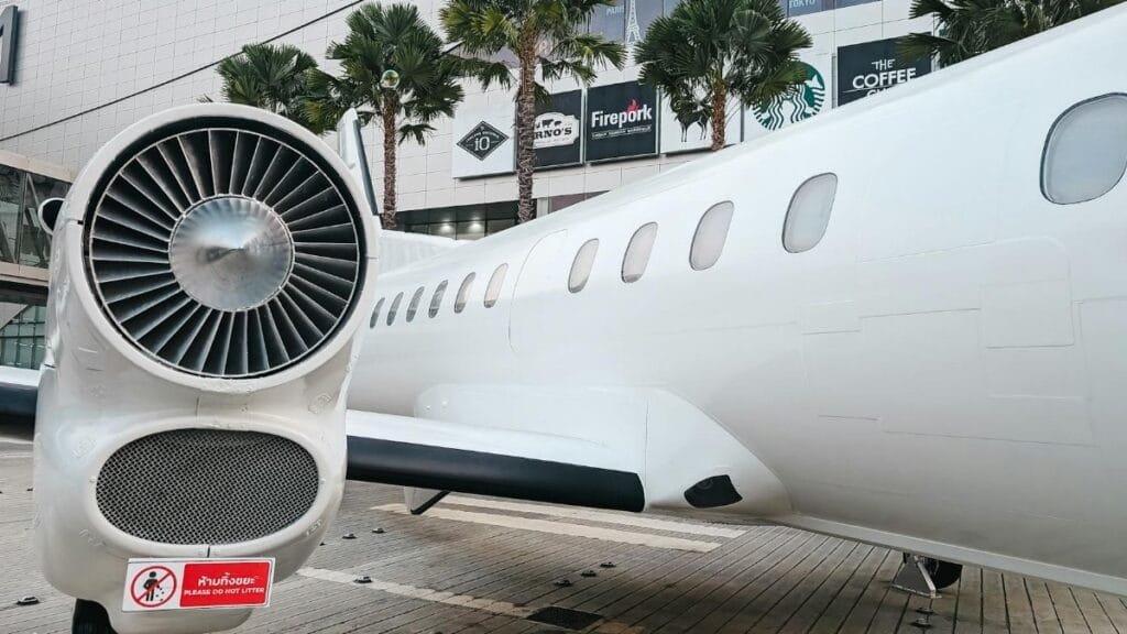 Private jet parked at a modern airport terminal with palm trees and shopping signs visible.