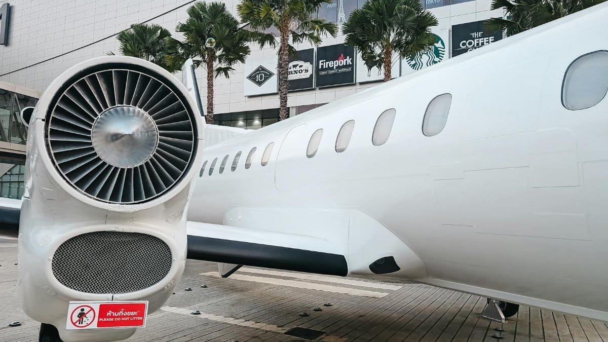 Private jet parked at a modern airport terminal with palm trees and shopping signs visible.