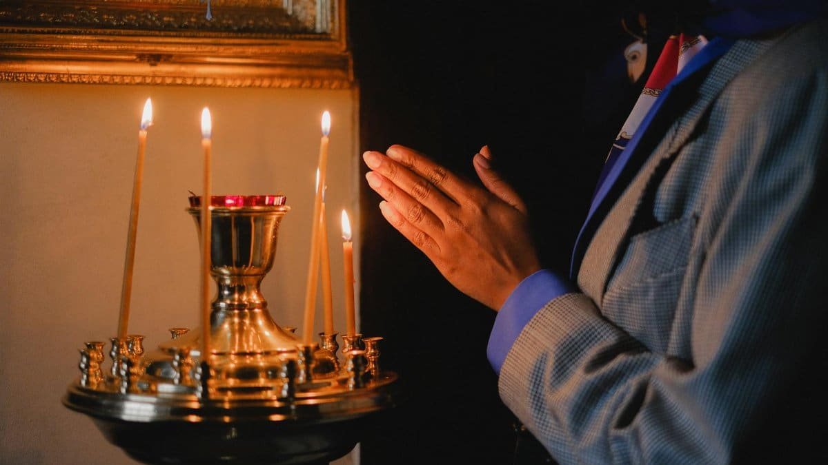 A person praying beside lit candles in a religious setting, evoking peace and spirituality.