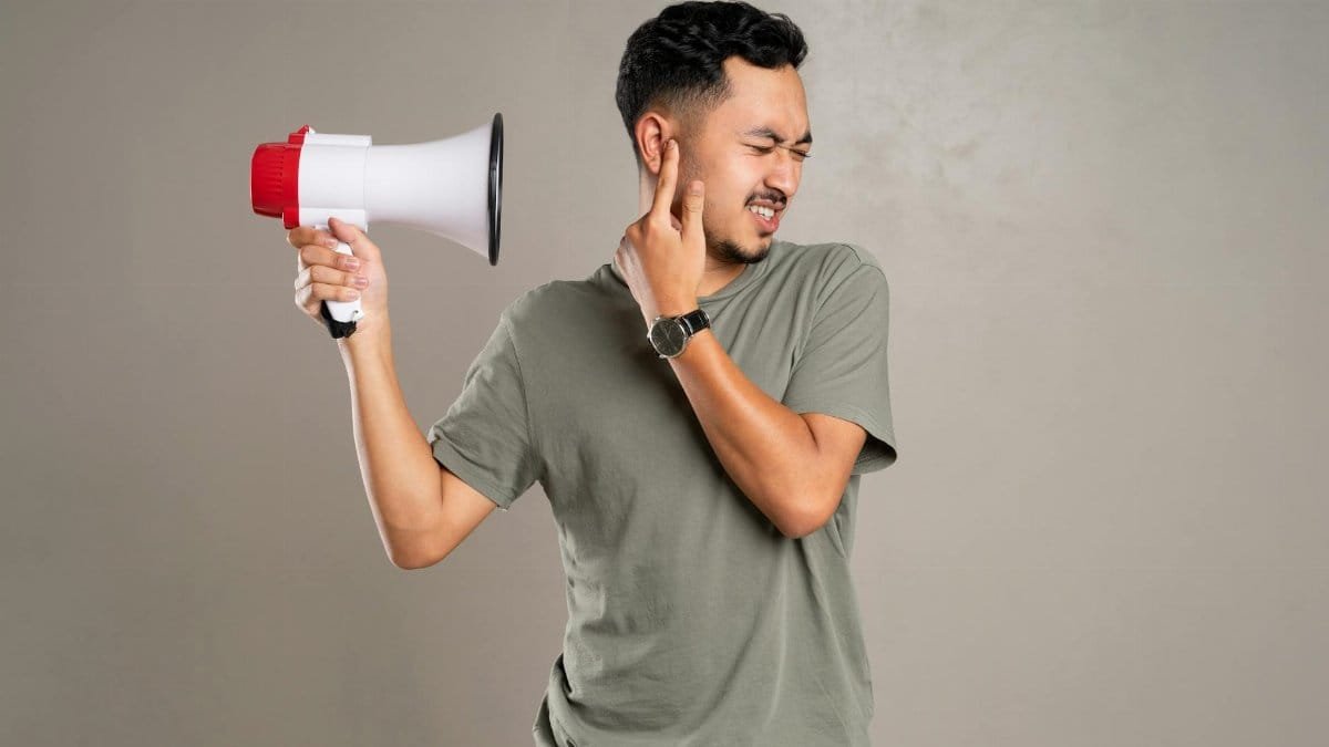 A man with a megaphone holding ear in discomfort, representing noise pollution or loud sounds.