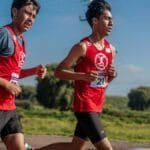 Two young men running in a marathon through the countryside, showcasing endurance and fitness.