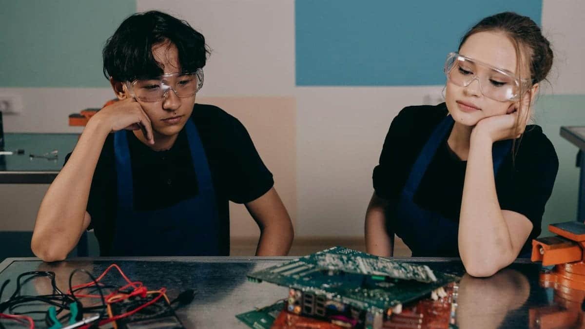 Two young engineers studying electronic circuit boards in a workshop setting.