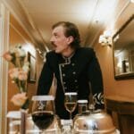 Hotel porter in vintage uniform delivering room service in a luxurious hallway.