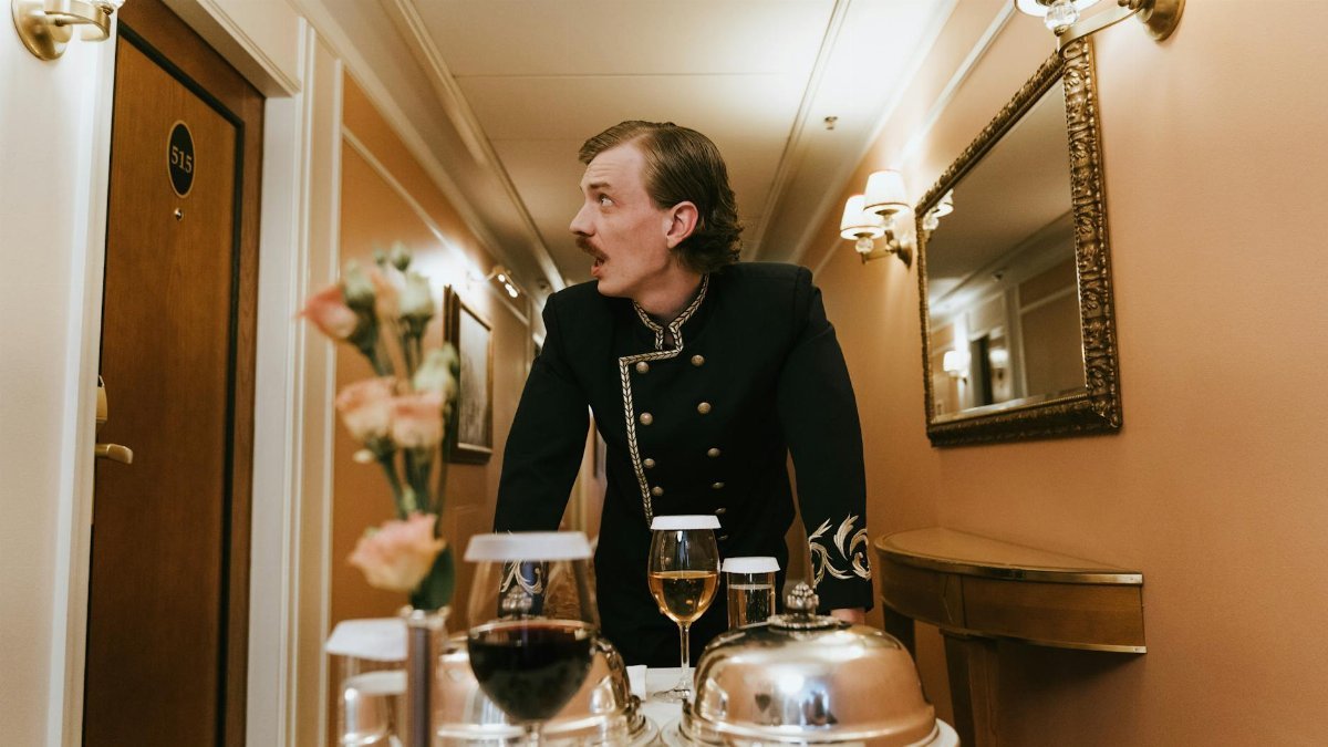Hotel porter in vintage uniform delivering room service in a luxurious hallway.