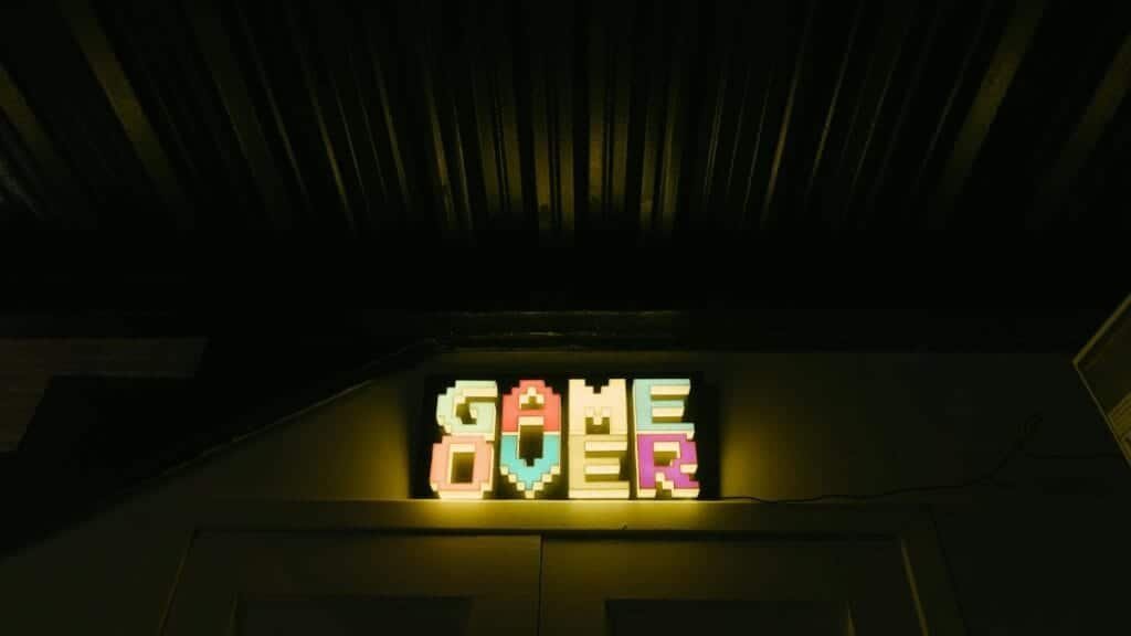 Glowing neon sign with pixelated Game Over text in a dark arcade setting.