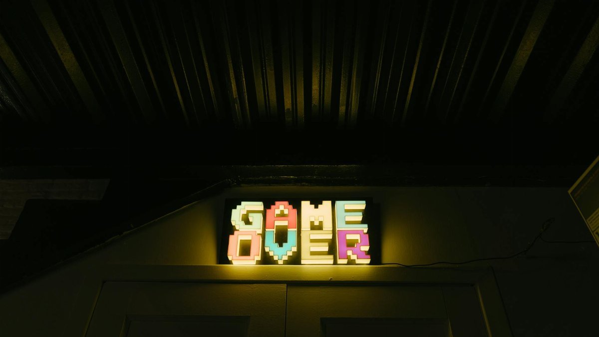 Glowing neon sign with pixelated Game Over text in a dark arcade setting.