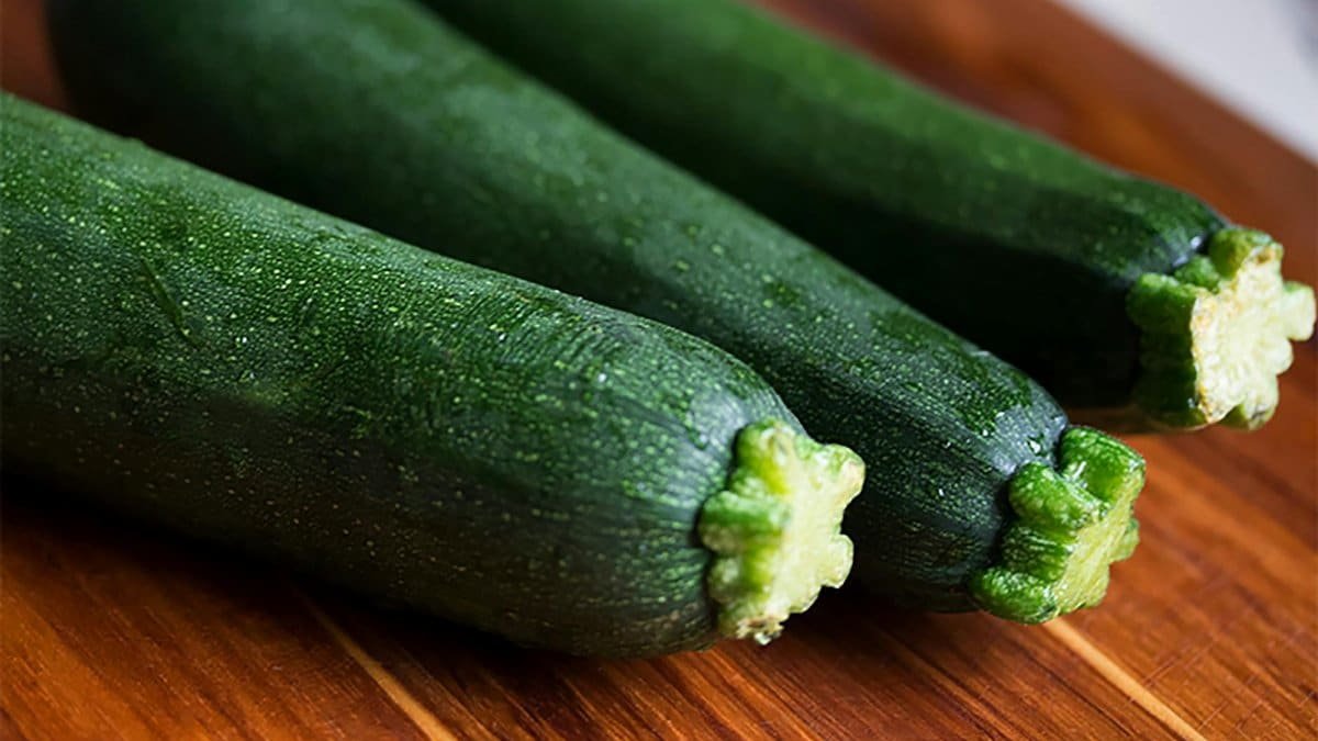 Close-up of three fresh green zucchinis on a wooden surface, perfect for food themes.