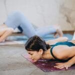 Two women perform yoga poses indoors, focusing on strength and mindfulness.